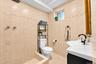 Full-wall neutral tile with decorative inlay, walk-in shower area, pedestal-style sink with matte black faucet, and recessed ceiling lighting