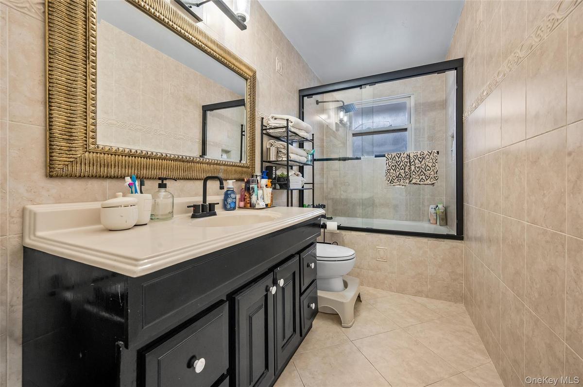 Black vanity cabinet with a solid surface countertop, matte black faucet, and tiled shower enclosure with a glass door