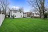 Expansive backyard featuring a level lawn, white vinyl fencing, mature trees, and a paved stone patio