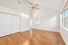 Vaulted ceiling featuring a central lighted ceiling fan, wood-finish flooring, multi-panel bi-fold closet doors, and large windows with natural light