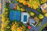 Aerial perspective of dual tennis courts and a swimming pool with a hardscape deck, surrounded by mature deciduous trees