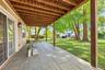 Covered patio featuring large-format stone-style pavers, exposed wood ceiling beams, sliding glass doors, and direct access to a lawn with mature tree
