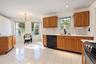 Kitchen featuring white tile flooring, wood cabinetry, stone-style backsplash, integrated matte black faucet, and recessed lighting