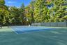Tennis court featuring a blue surface, full-perimeter chain-link fencing, and mature tree-lined borders
