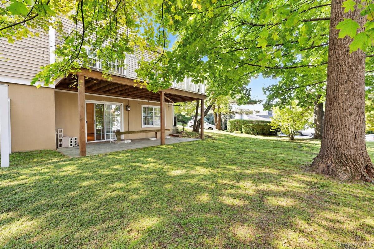 Backyard featuring a paved patio, a wood-framed elevated deck, siding exterior, sliding glass doors, and mature trees
