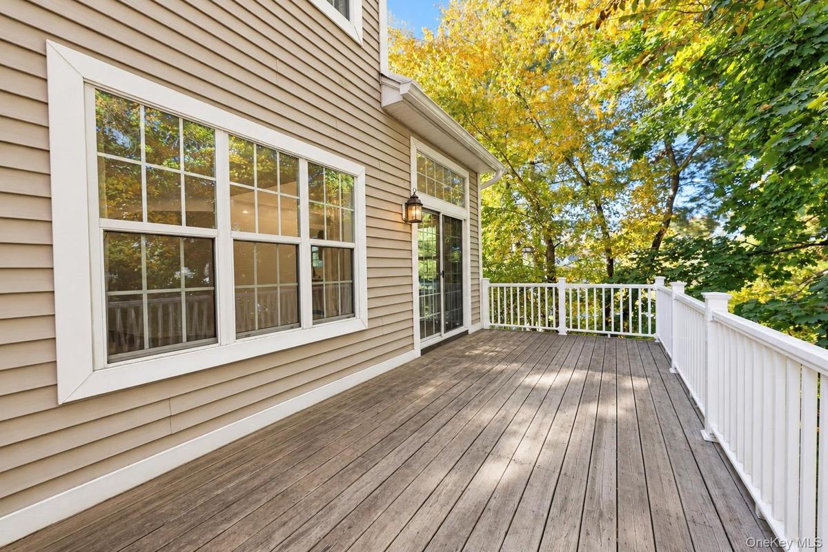 Exterior deck featuring wood-finish plank flooring, white balustrade railings, neutral horizontal siding, and glass sliding doors with multi-light win