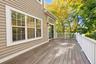 Exterior deck featuring wood-finish plank flooring, white balustrade railings, neutral horizontal siding, and glass sliding doors with multi-light win