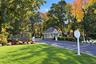 Gated entrance featuring a stone-clad guard house, asphalt driveway, automated security barrier, and professional landscaping