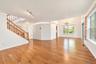 Open floor plan featuring wood-finish flooring, vaulted ceilings, a central staircase with wooden railings, multi-light track lighting, and decorative
