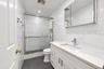Bathroom featuring a white vanity with a composite countertop, undermount sink, mirrored medicine cabinet, glass-enclosed shower with tiled walls, and