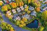 Aerial perspective of a residential neighborhood featuring mature deciduous trees, paved roadways, and a central pond