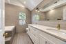 Bathroom featuring a dual-sink vanity with white shaker-style cabinetry, quartz countertops, and brass-finish fixtures, complemented by full-height ce