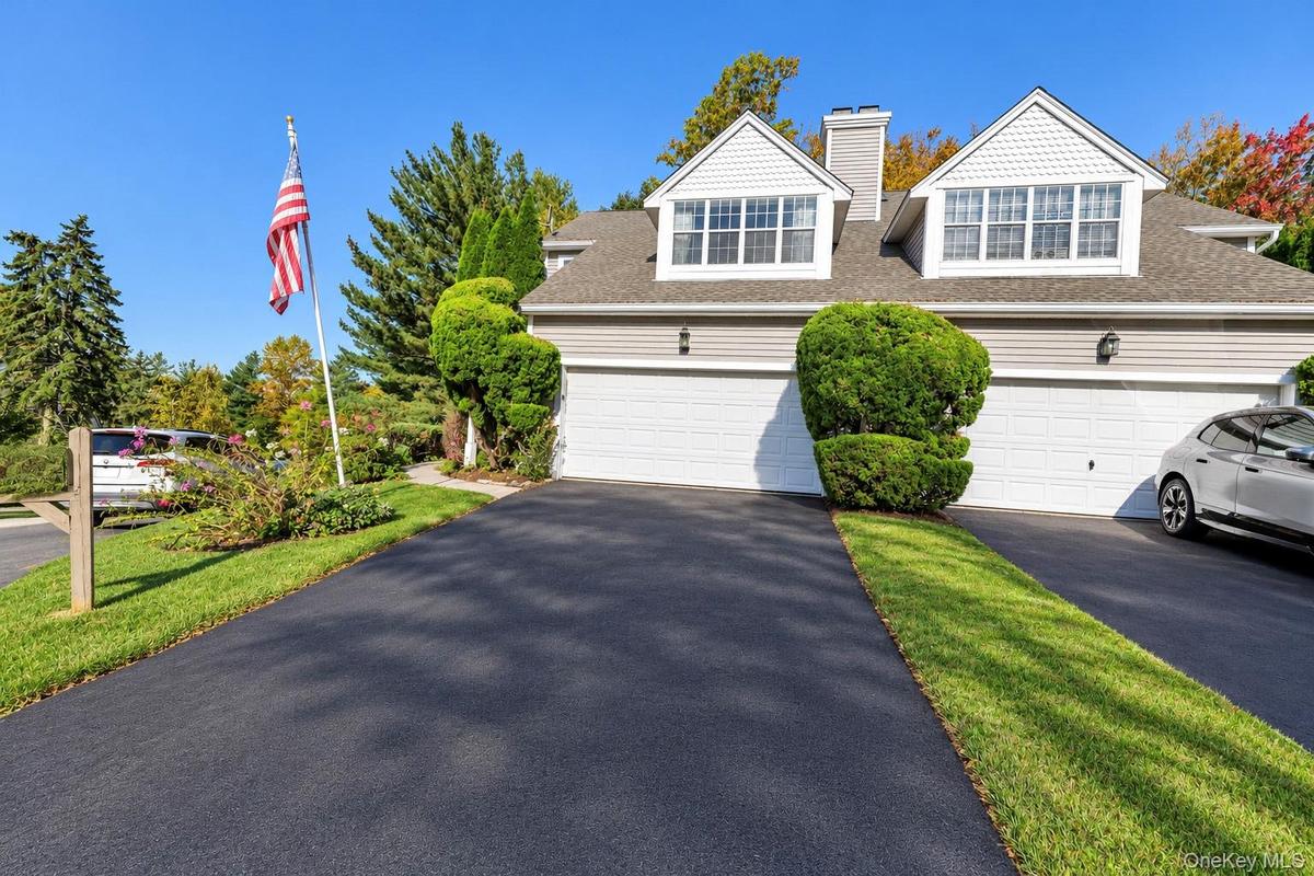 Two-story exterior featuring dual dormer windows, horizontal siding, an attached two-car garage, and asphalt driveway