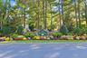 Stone monument signage with professional landscaping featuring mature trees, manicured lawn, and varied shrubbery