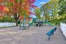 Recreational area featuring a playground structure with dual slides, metal perimeter fencing, and established shade trees