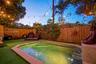 Backyard featuring a custom-shaped pool with integrated stairs, perimeter stone coping, vertical wood privacy fencing, and overhead string lighting