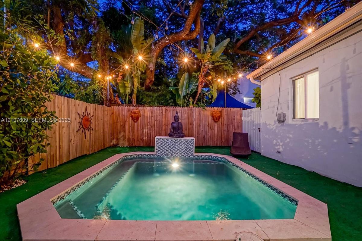 Private rear grounds featuring a custom swimming pool with patterned tile water feature, perimeter wood privacy fencing, and mature tropical landscapi