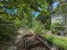 Outdoor area featuring wood-framed garden beds, natural landscape elements, mature trees, and vinyl siding