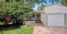 Single-story exterior featuring a paver driveway, attached garage, covered front porch, and mature landscaping