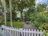 Private backyard featuring a white picket fence, mature trees, manicured lawn, and a crushed stone ground cover