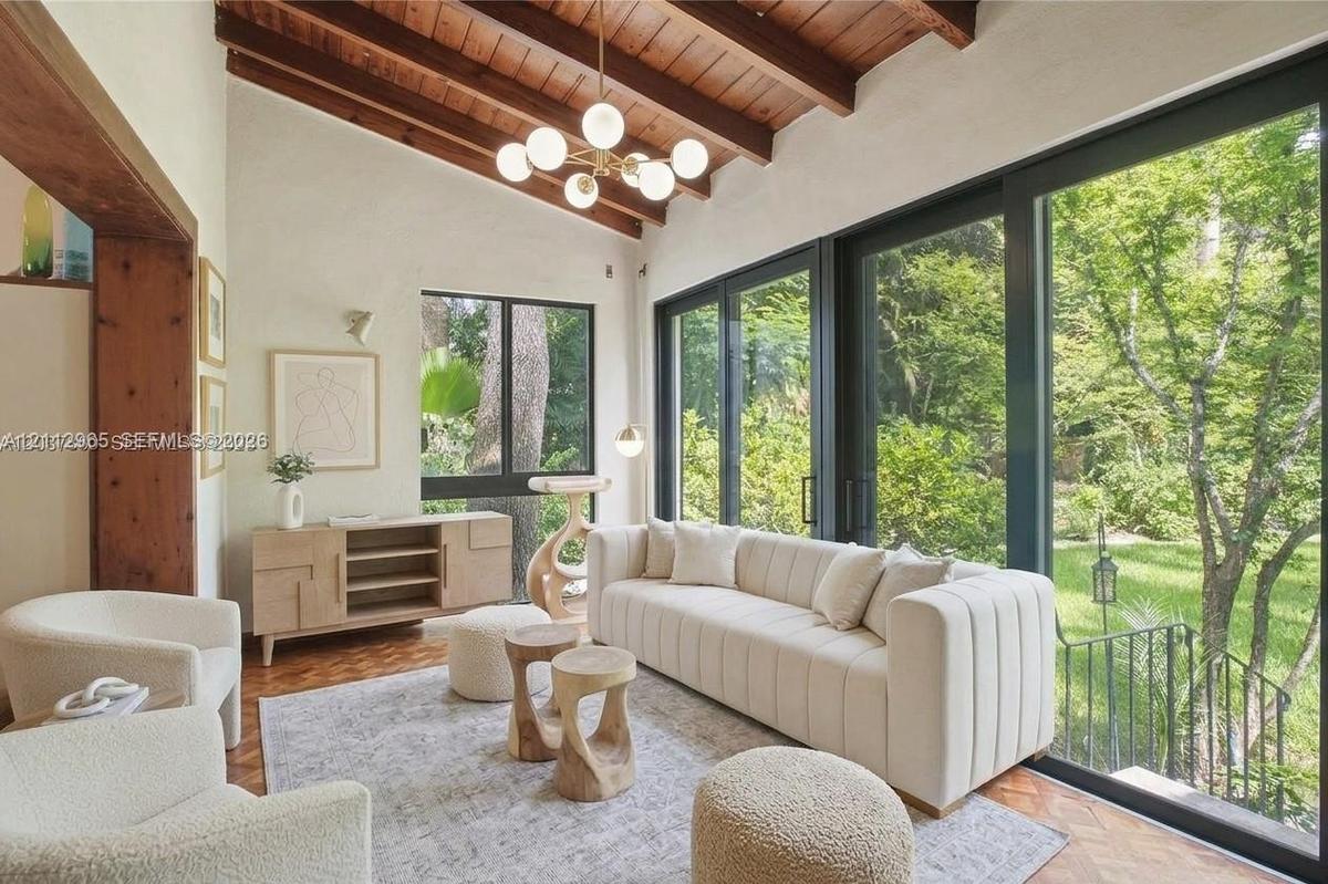 Vaulted ceiling with exposed wood beams, sliding glass walls, herringbone-patterned wood-finish flooring, and multi-globe chandelier