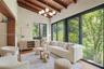 Vaulted ceiling with exposed wood beams, sliding glass walls, herringbone-patterned wood-finish flooring, and multi-globe chandelier