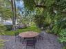 Expansive backyard featuring a stone-aggregate patio, lush lawn, and mature canopy trees