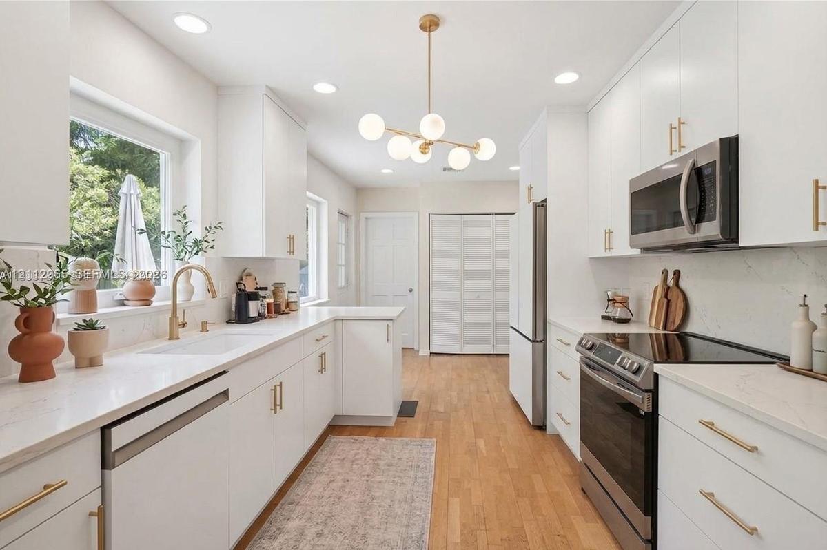 Kitchen featuring white cabinetry with gold-toned hardware, solid-surface countertops, wood-finish flooring, stainless steel appliances, and a modern 