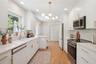 Kitchen featuring white cabinetry with gold-toned hardware, solid-surface countertops, wood-finish flooring, stainless steel appliances, and a modern 