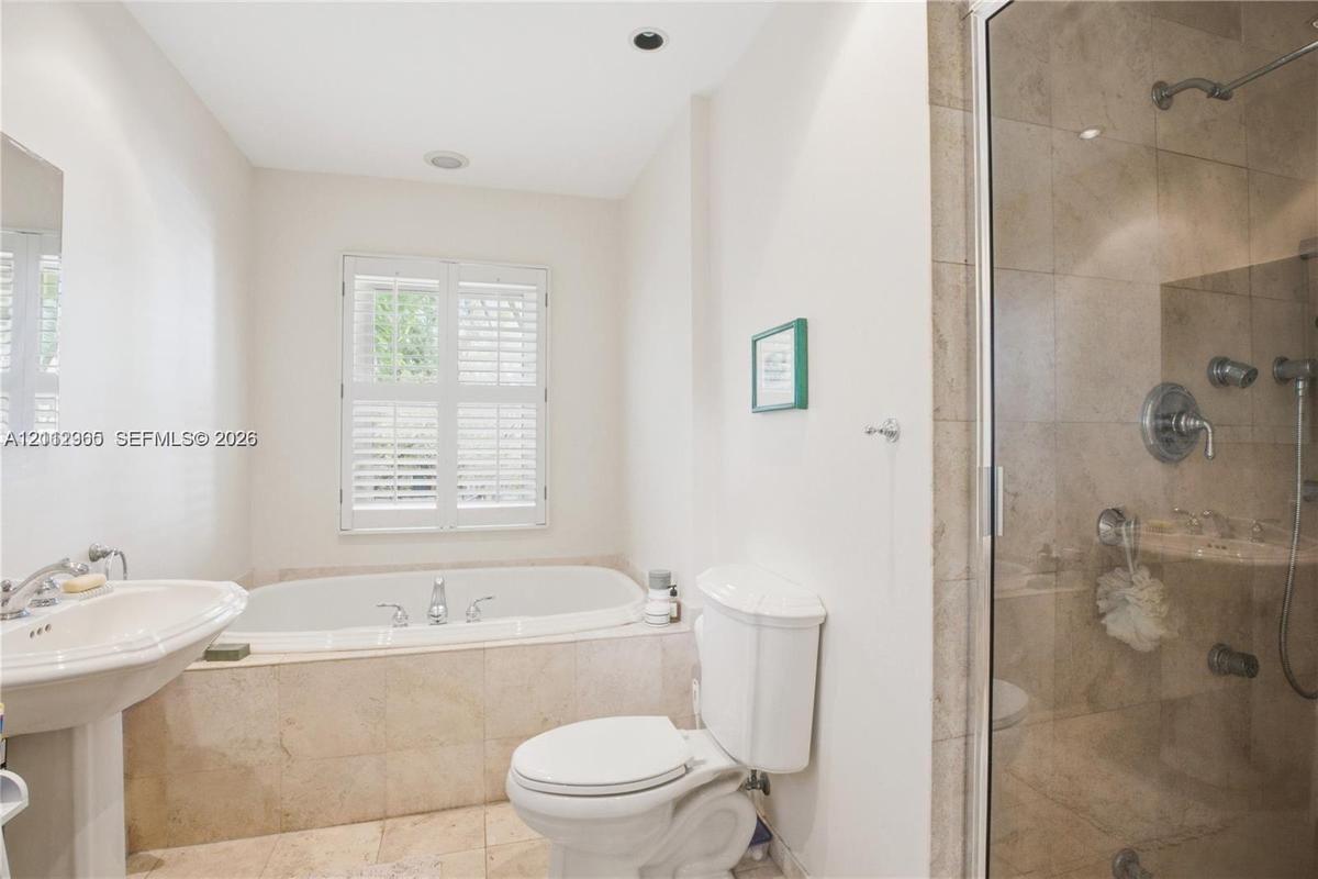 Bathroom featuring a pedestal sink, soaking tub with tile surround, glass-enclosed shower with metallic fixtures, and plantation shutters