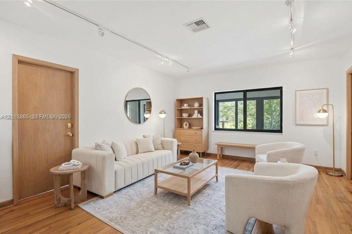 Living space featuring wood-finish flooring, white walls, track lighting, and black-framed windows