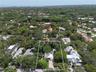 Aerial perspective of a property featuring a paved driveway, mature tree canopy, and substantial lot coverage, situated within a coastal-adjacent land