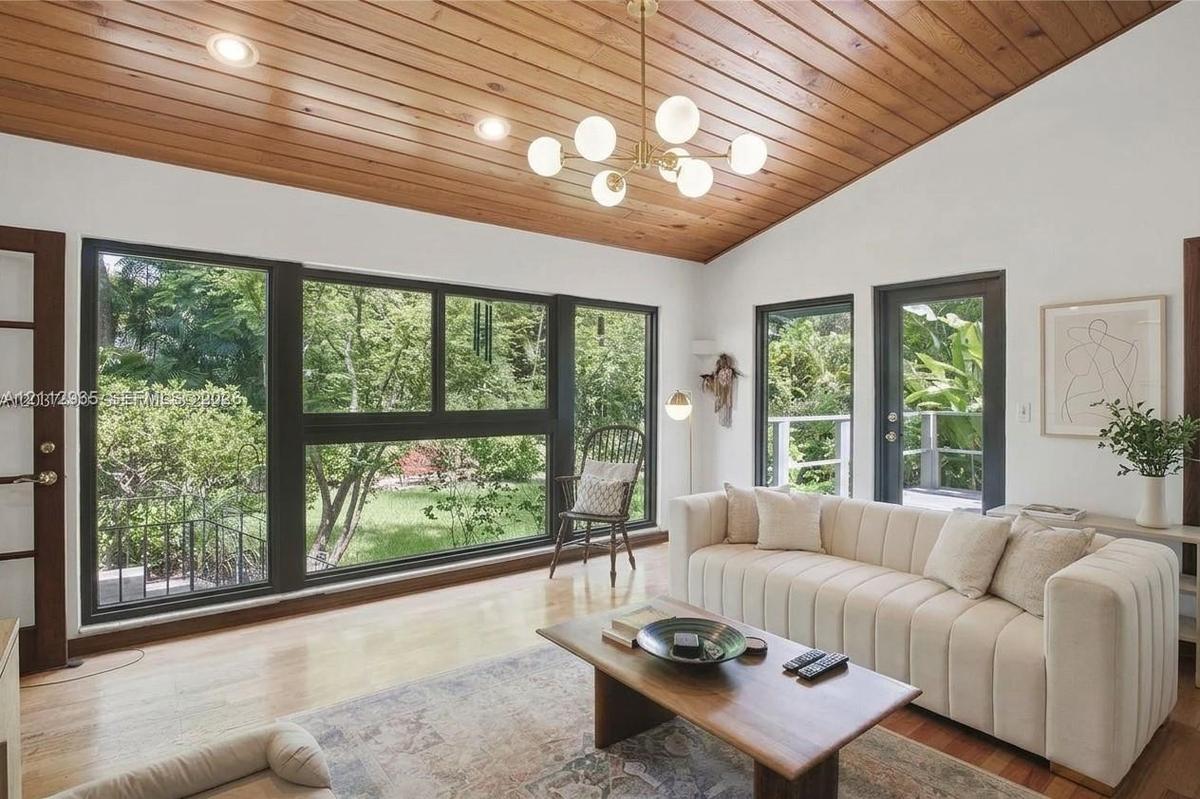 Vaulted wood-plank ceiling featuring a multi-light globe chandelier, expansive floor-to-ceiling windows with black framing, and light-toned wood-finis