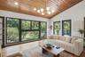 Vaulted wood-plank ceiling featuring a multi-light globe chandelier, expansive floor-to-ceiling windows with black framing, and light-toned wood-finis