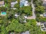 Aerial perspective of a property featuring solar panels, a paved driveway, and mature landscaping with expansive tree canopy