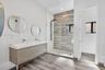 Double vanity with integrated sinks, wall-mounted faucets, wood-finish cabinetry, walk-in shower with horizontal tile surround, and wood-finish floori