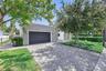 Detached garage with large-format stone-textured exterior cladding, paved brick driveway, metal gate, and manicured landscaping