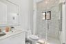 Modern bathroom featuring a white vanity with an integrated countertop, wall-mounted mirror, walk-in shower with a glass enclosure, patterned tile sho