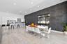 Modern kitchen and dining area featuring high-gloss white cabinetry, expansive stone tile flooring, a dark charcoal textured accent wall, recessed lig