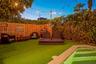Private outdoor space featuring synthetic lawn, pool with a stone coping border, perimeter wood fencing, and overhead string lighting