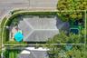 Aerial perspective featuring a shingle roof, a rectangular inground pool, expansive stone-paver hardscaping, mature perimeter hedges, and established 