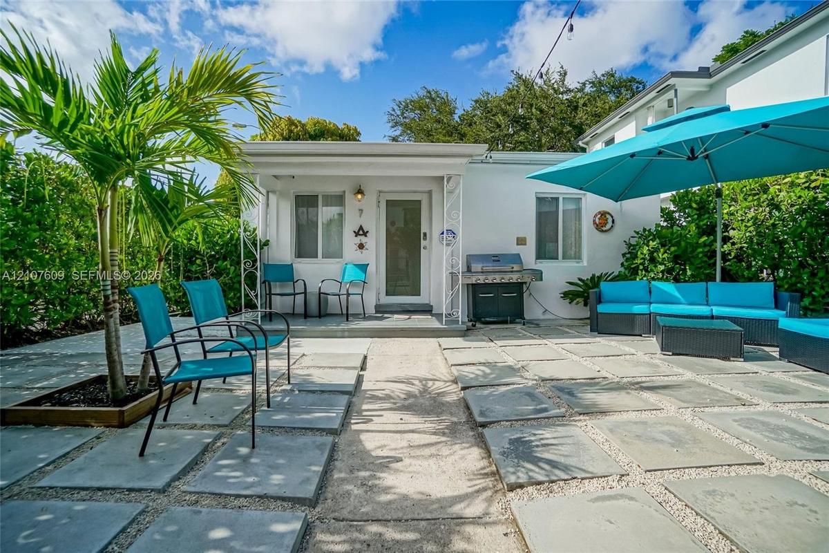 Enclosed patio featuring large-format concrete pavers, gravel infill, ornamental metal porch supports, and mature palm tree landscaping