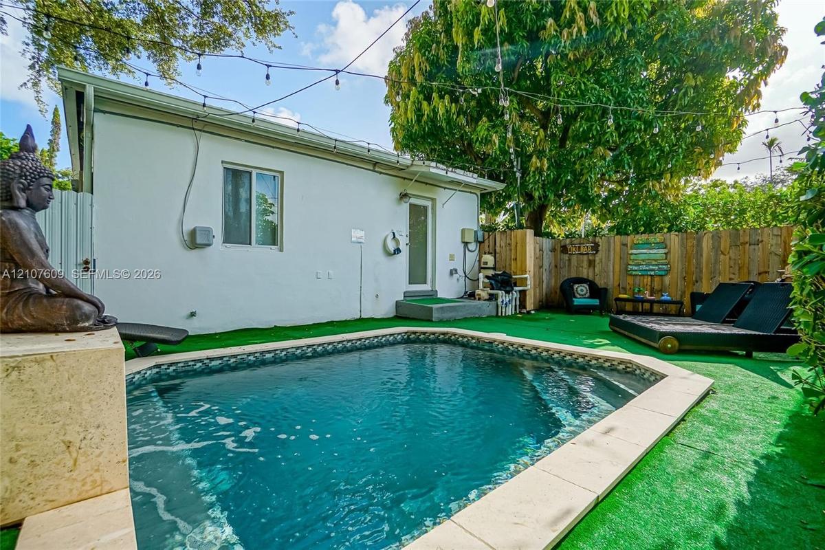 Backyard area featuring an in-ground pool with stone coping, synthetic grass surfacing, and wood-panel privacy fencing