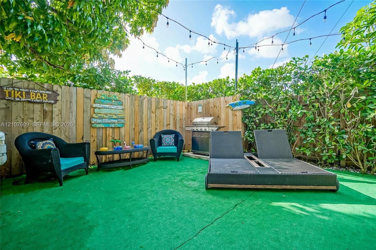 Fenced backyard featuring wood-plank fencing, built-in outdoor grill, and overhead string lighting