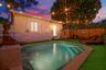 Backyard featuring an in-ground pool with stepped entry, stone-finish coping, synthetic turf ground cover, and perimeter wood privacy fencing