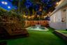 Backyard featuring a geometric swimming pool with tiled water feature, artificial turf surfacing, perimeter wood fencing, and mature landscaping