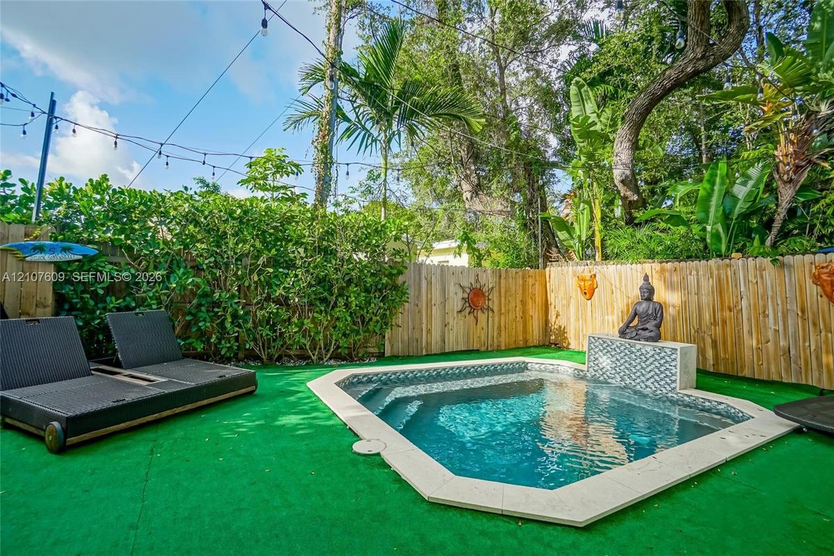 Backyard area featuring an in-ground swimming pool, stone-tile coping, integrated water feature with patterned inlay, wood privacy fencing, and overhe