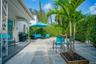 Rear patio featuring concrete paver hardscaping, white exterior walls, decorative metal porch pillars, and a dedicated garden bed with a mature palm