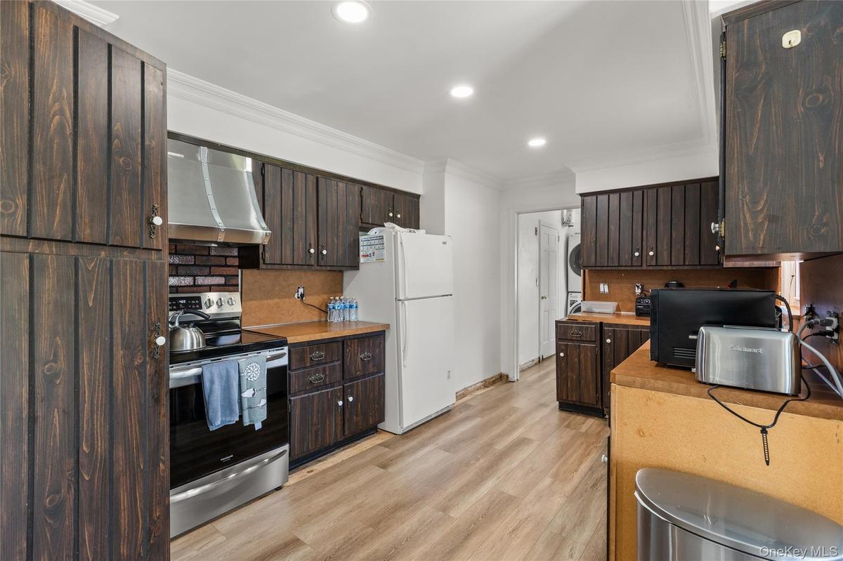 Kitchen with dark brown cabinetry, crown molding, electric range, ventilation hood, and tasteful backsplash