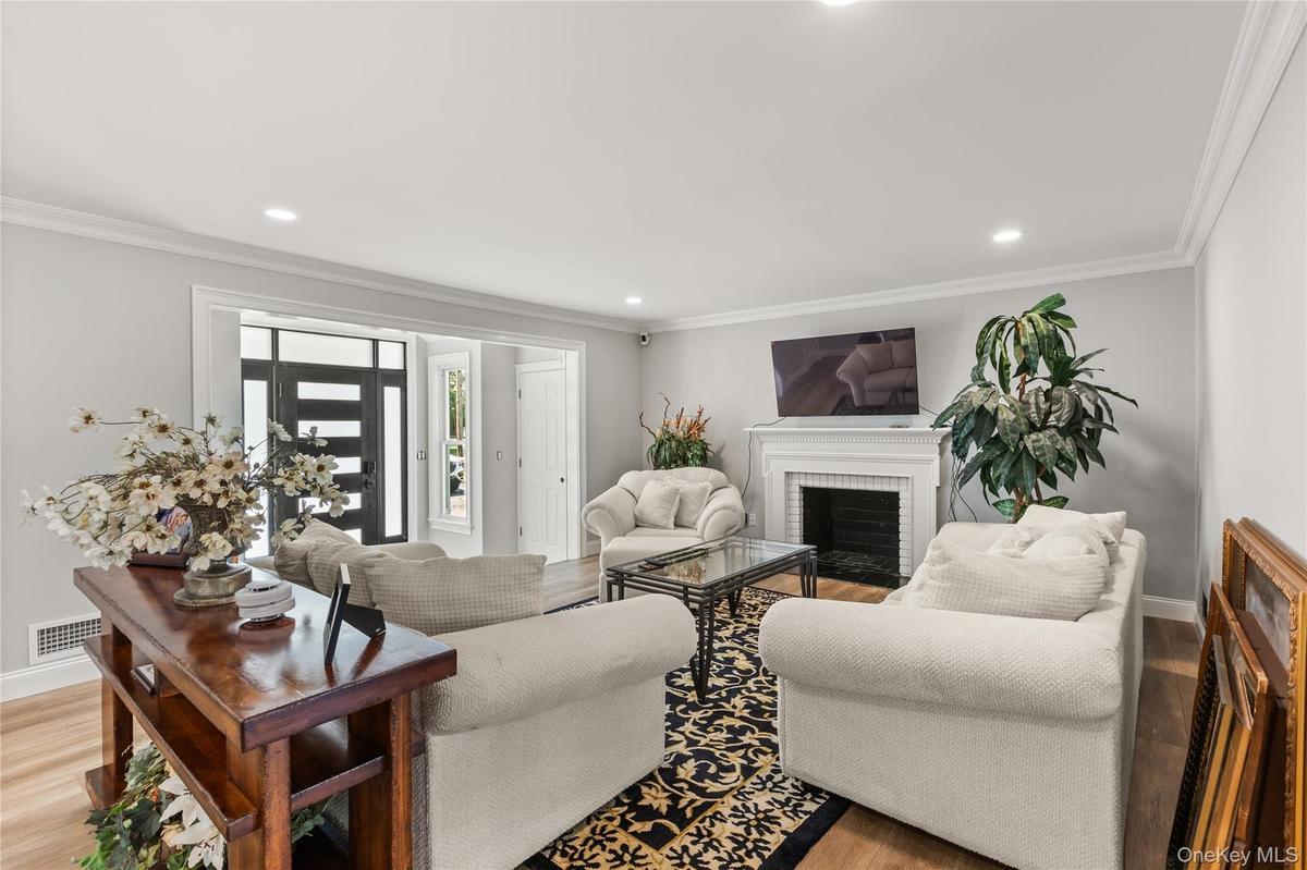 Living area featuring light wood-style flooring, a brick fireplace, crown molding, and recessed lighting